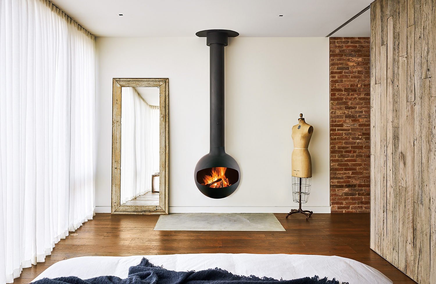 Bathyscafocus sphere hanging at the foot of a bed beside a full-length mirror and brick wall