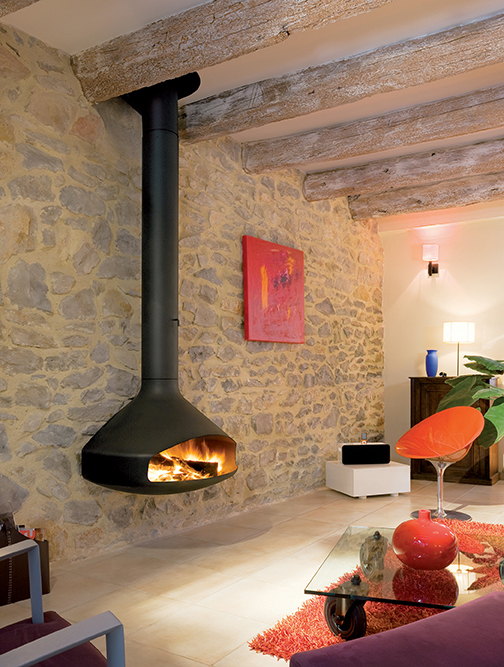 Black Paxfocus wall-backed fireplace burning against a rustic stone wall beside an orange chair