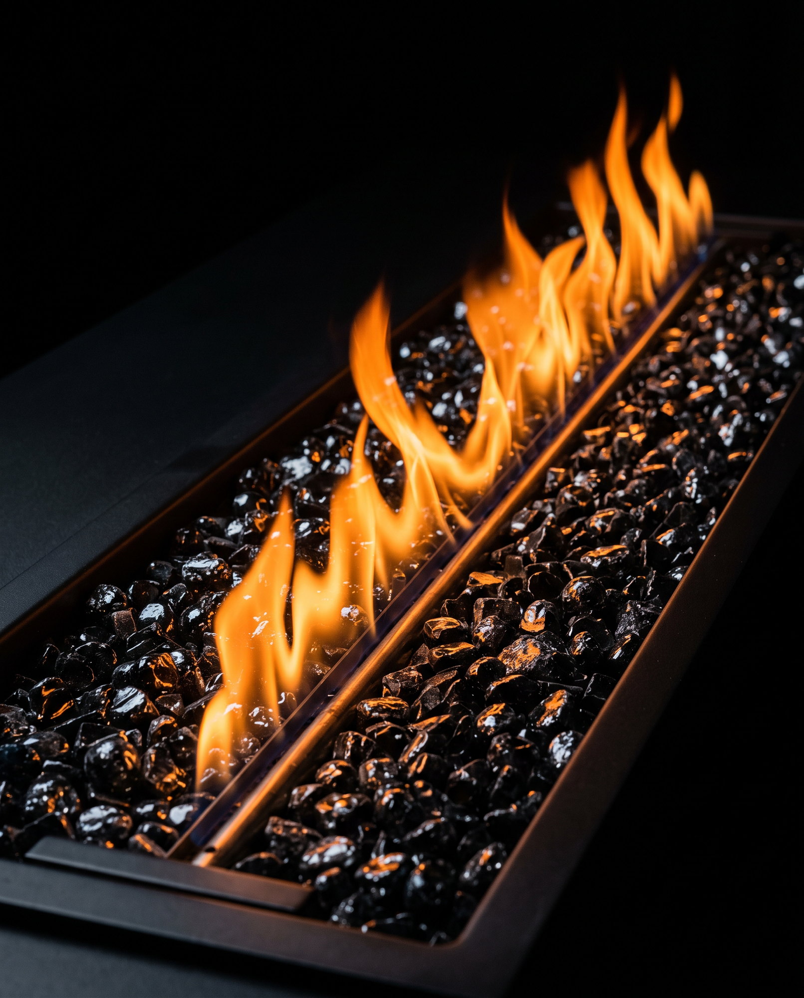 A ribbon of steady gas flame rising through black glass media in a linear burner tray