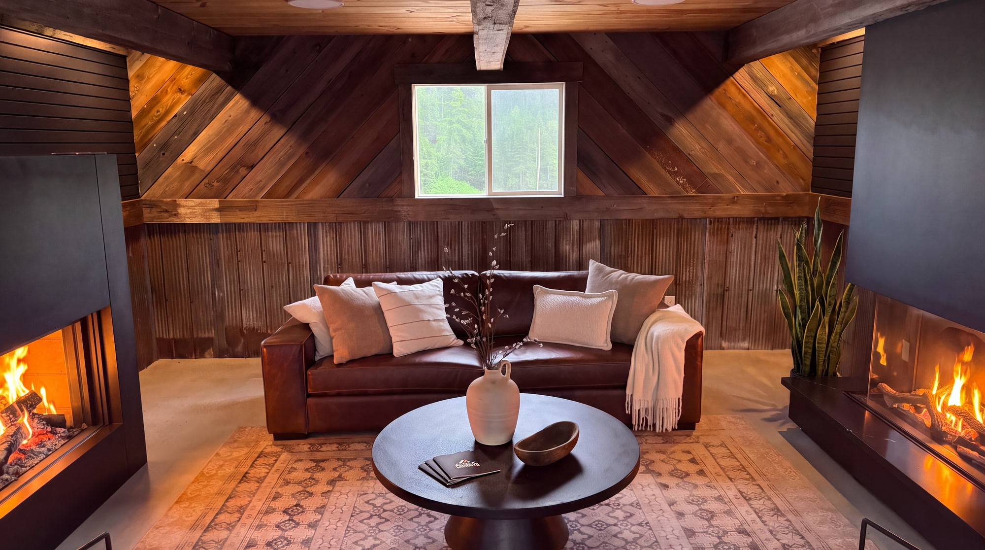 The barnboard den at the Chase N’ Chimneys showroom: a leather couch with a burning fireplace on either side of it — a Stûv 21-125 on the left and an Urbana on the right — under a beamed ceiling