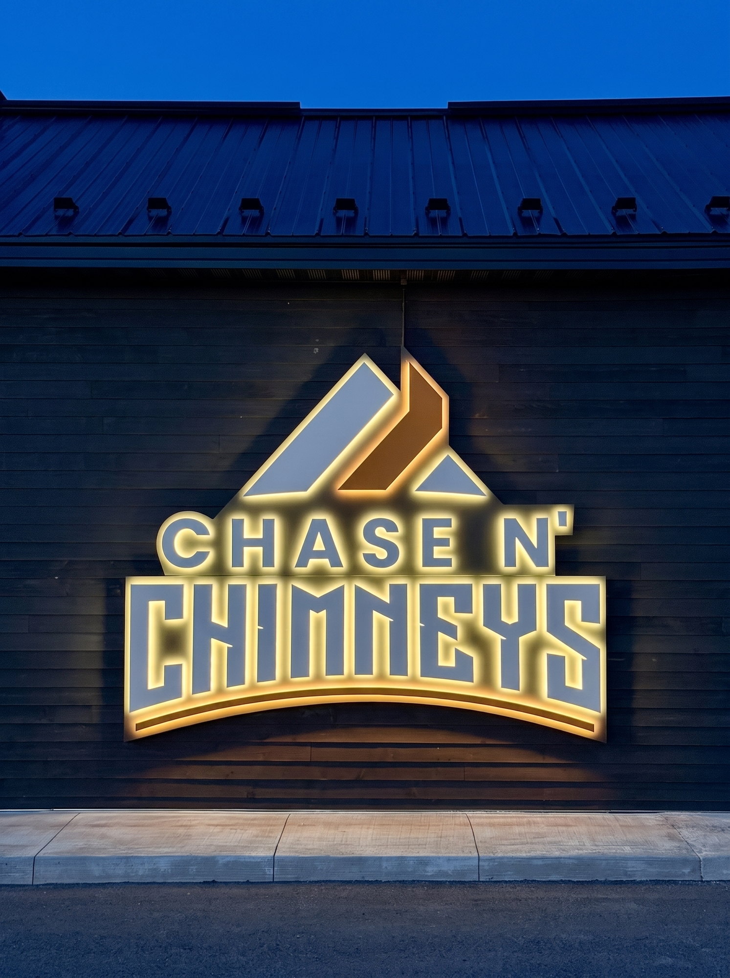 The Chase N’ Chimneys sign glowing warm at dusk on the dark wood-clad building