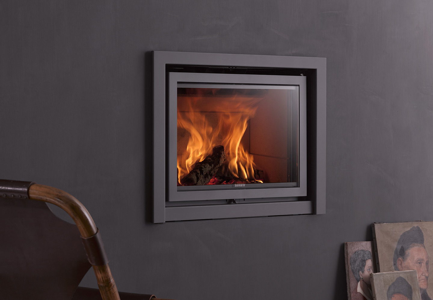 Stûv 16-in insert burning flush in a charcoal wall, a painting leaning beside it
