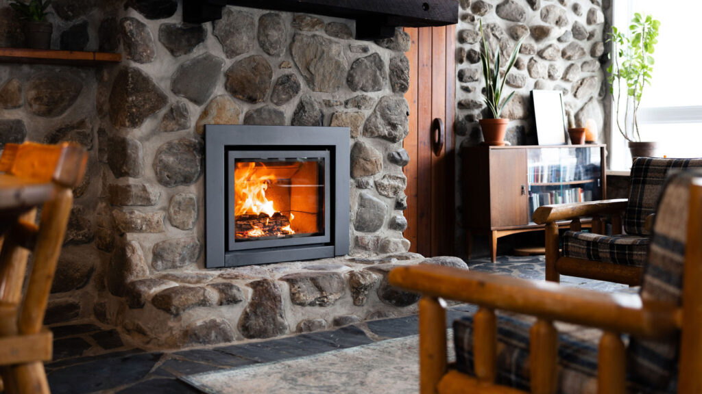 The Stûv 16-in burning in a round-stone chimney inside a Canadian log cabin