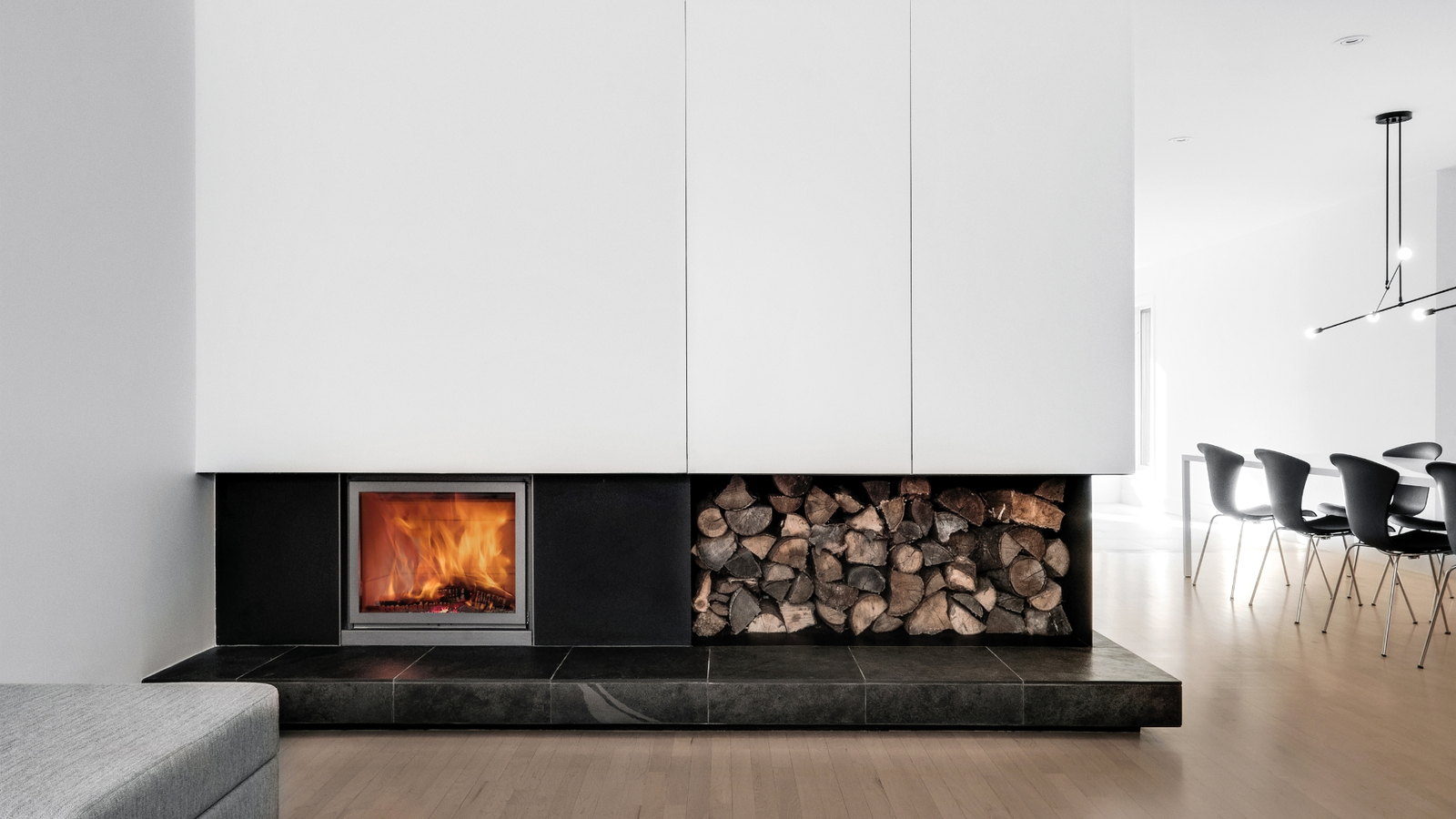 Stûv 16-Z in a white volume over a black stone bench, firewood stored alongside