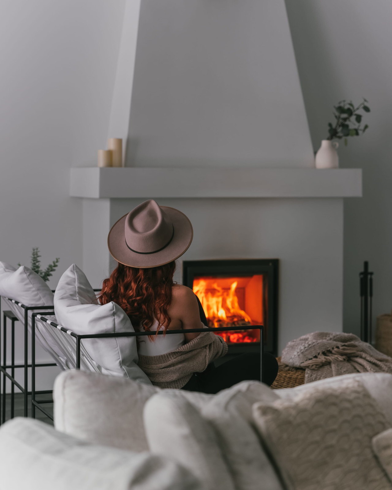 The Stûv 16-Z alight in a white plaster chimney, a reader settled close by