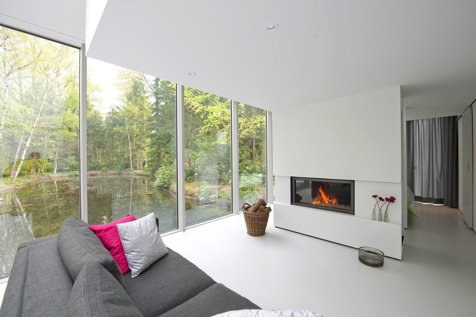 Stûv 21 with its glass raised, burning in an all-white lakeside living room