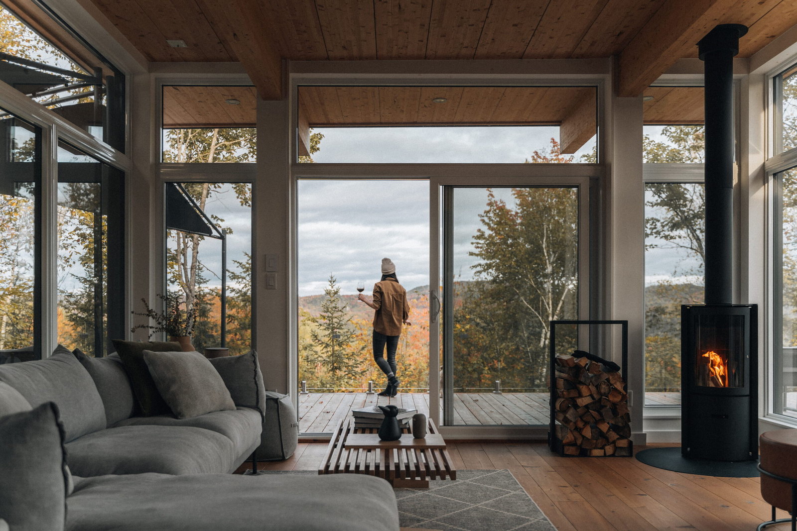 The jet-black Stûv 30-Compact ONE burning in a glass-walled great room, log rack beside