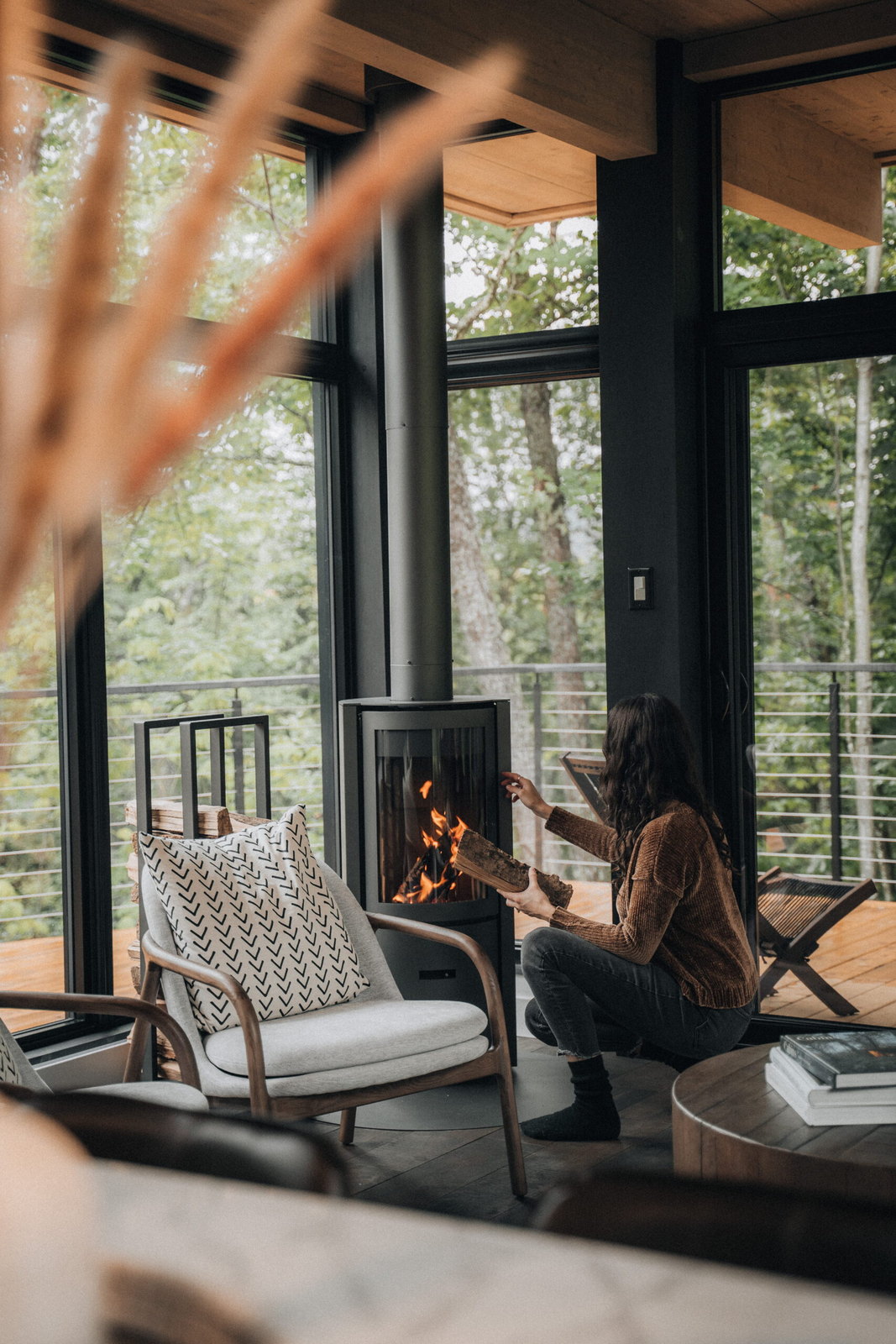 Hands warming by the Stûv 30-Compact, forest through the glass wall