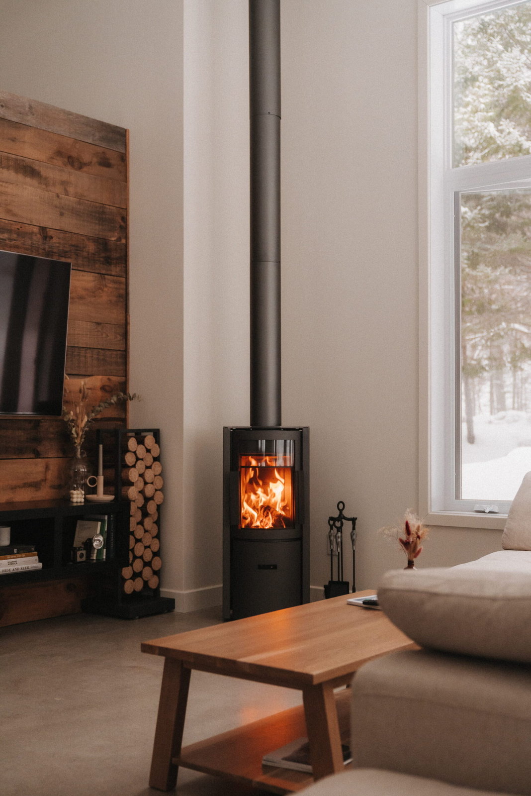 The Stûv 30-Compact burning against a barnwood wall, snow out the window