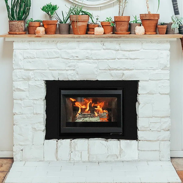 The Stûv 6-in burning in a whitewashed brick chimney under a mantel of potted terracotta