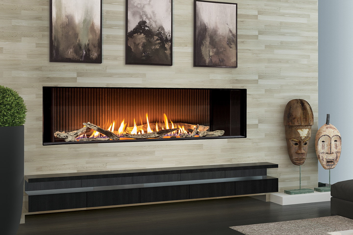 Urbana U70 Tall Linear gas fireplace running along a pale stone wall between carved masks
